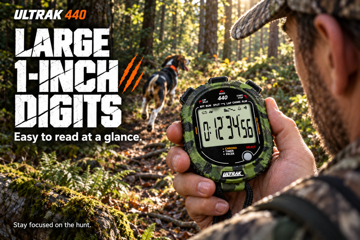 A person in camouflage clothing holds a camouflage-patterned ULTRAK 440 digital stopwatch outdoors in a forest, with a dog in the background. Large promotional text on the left reads 'ULTRAK 440 LARGE 1-INCH DIGITS Easy to read at a glance.