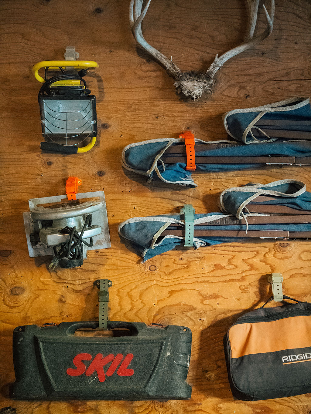 Tools including a SKIL case, Ridgid bag, and other equipment on a wooden surface with antlers.