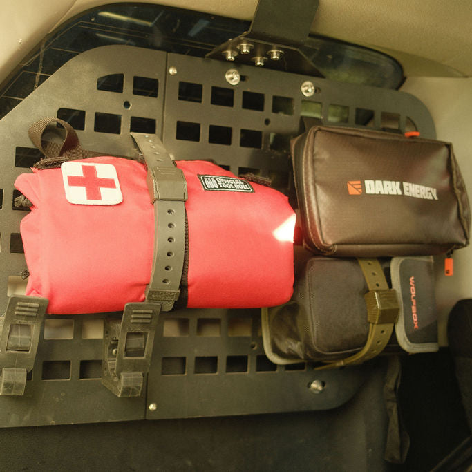 A red rolled emergency blanket with a white cross patch and a black DArk Energy pouch mounted on a black vehicle cargo rack.
