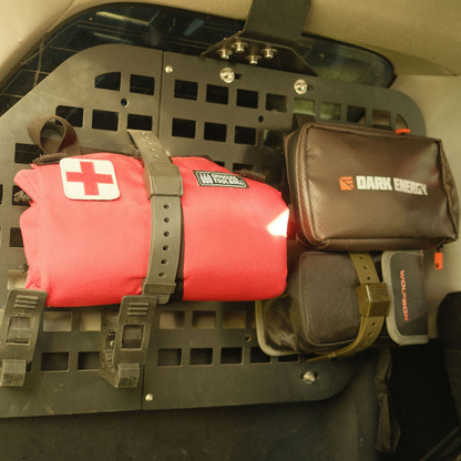 A red rolled emergency blanket with a white cross patch and a black DArk Energy pouch mounted on a black vehicle cargo rack.