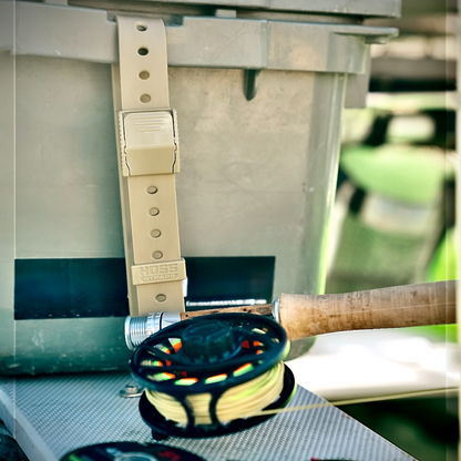 Fishing reel with a beige strap attached to a metal container outdoors.