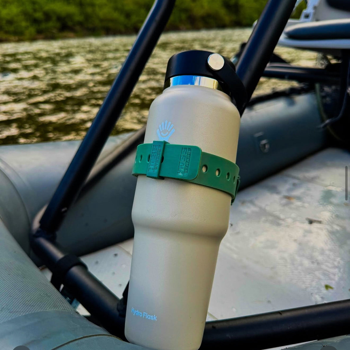 A beige insulated water bottle with a black cap and a green strap, mounted on a black frame inside a boat. The bottle has a blue wave logo and the text 'InnoFlask' near the bottom.